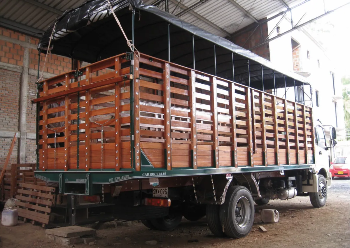 Camión con carrocería de estacas en madera y carpa negra en el taller